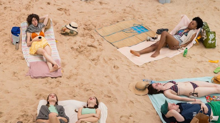 Persones estirades sobre tovalloles a la platja.