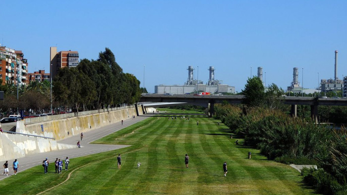 Esplanada de gespa amb persones caminant, a la vora del riu Besòs.