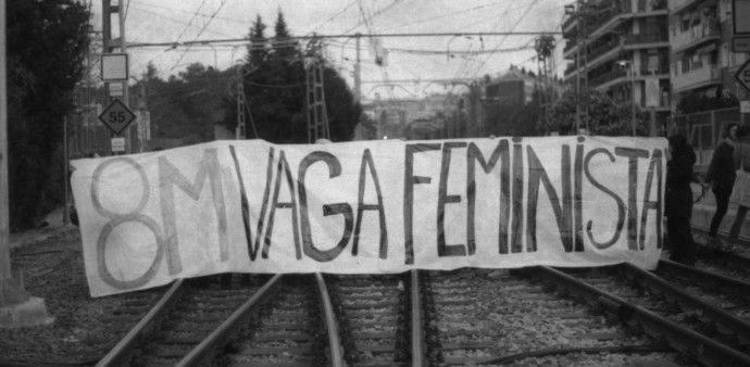 Manifestants subjectant una pancarta amb el lema "8M vaga feminista" a les vies del tren.